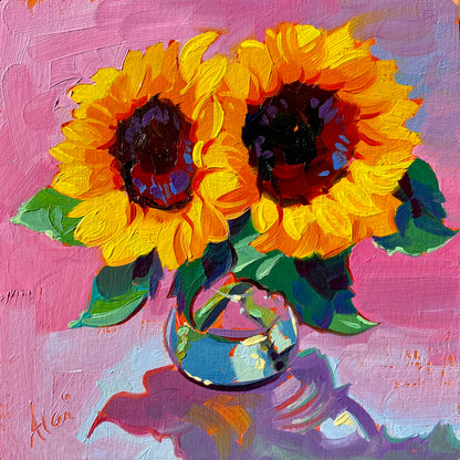 Original oil painting by Alai Ganuza titled "Sunflower Study". Two bright yellow and orange sunflowers sitting in a small clear glass vase, painted on a textured pink background on a square birch block.