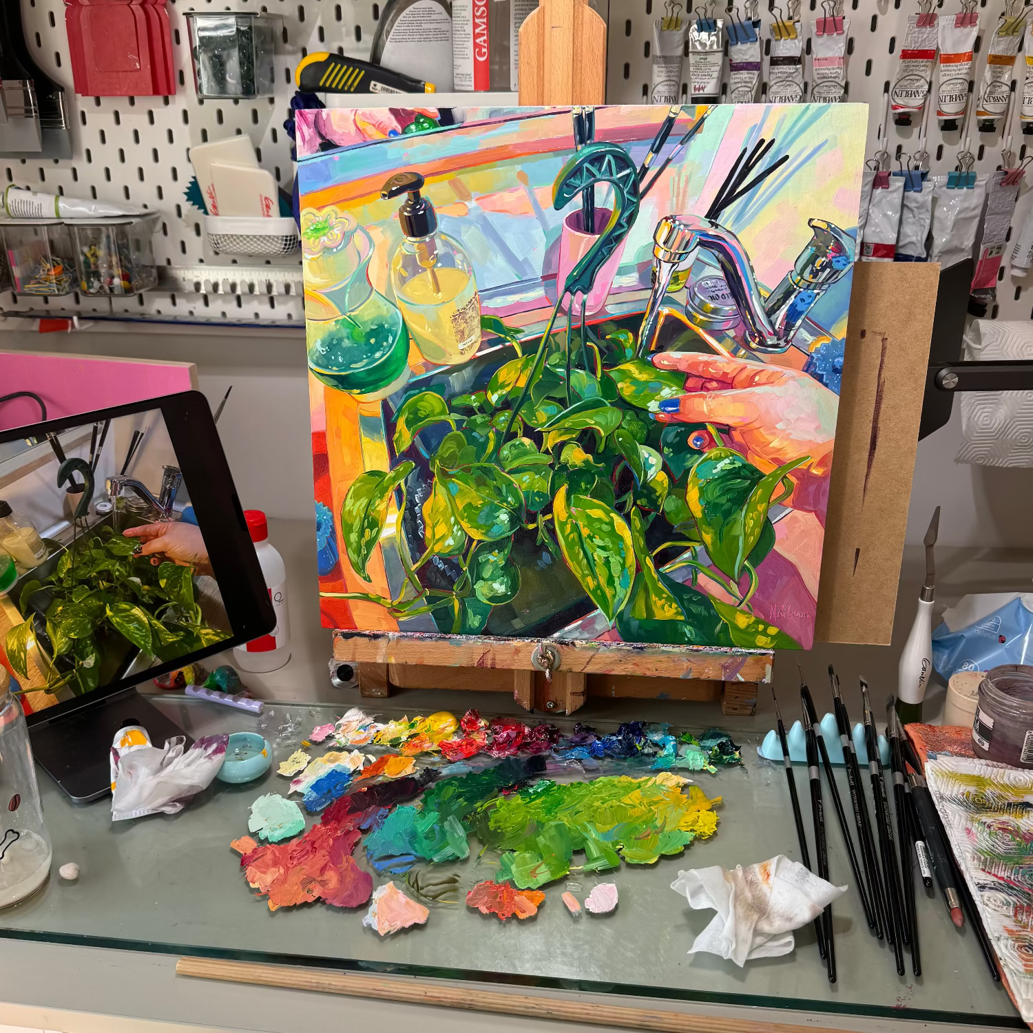 Original oil painting by Alai Ganuza depicting green houseplants beside glass bottles and a faucet, painted in vivid colors on an easel with a palette and brushes in the studio.