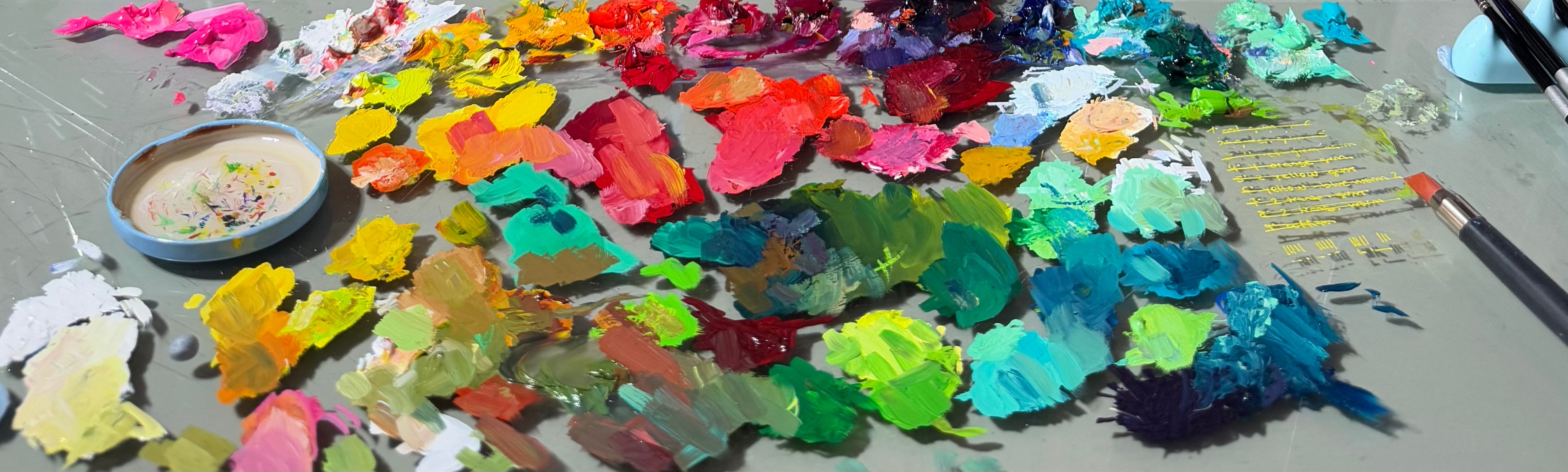 Colorful artist’s palette with vibrant oil paints in shades of yellow, pink, green, and blue, showing the creative process behind Alai Ganuza’s paintings.