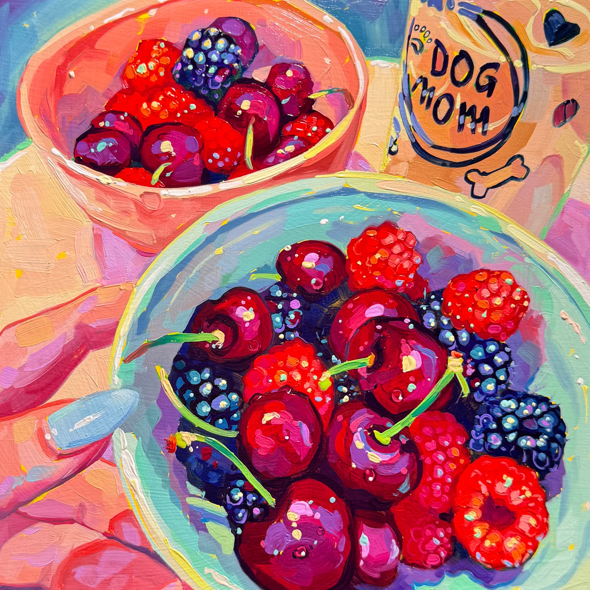 A square 20x20 cm original oil painting. In the center foreground, a clear bowl with a light teal rim is filled with deep red cherries, textured raspberries, and dark blue blackberries. A second, smaller pink bowl with more fruit sits just behind it to the left. In the upper right corner, a tan coffee mug is visible, featuring the words 'DOG MOM' in black script with a small heart. On the left edge, a hand with a single light blue painted fingernail rests near the bowl.
