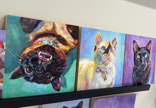 A collection of three 10x10 inch custom cat oil paintings displayed together, showing a cohesive palette of blue, teal, and purple with buttery paint applications.