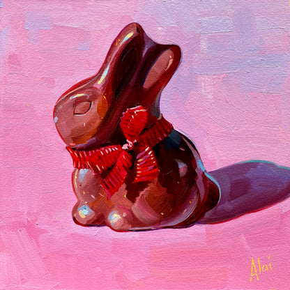 Original oil painting by Alai Ganuza titled "Chocolate Bunny". A glossy milk chocolate rabbit with a bright red ribbon tied in a bow, sitting against a textured pink background on a square aluminum panel. Reference by Leah Gardner.