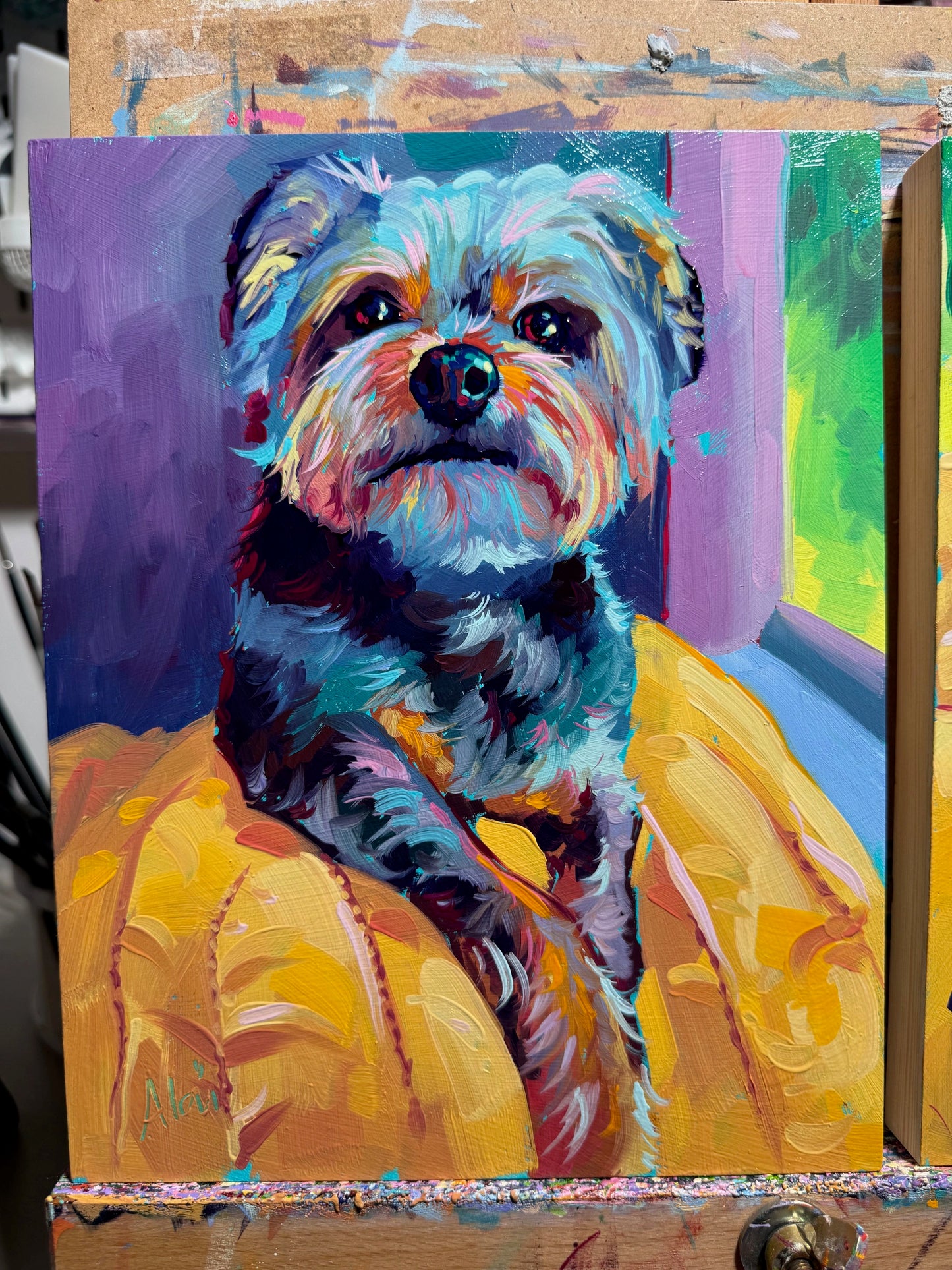A vibrant 8x10 oil painting of a scruffy dog named Maeby on a yellow blanket. It features rainbow-colored fur highlights, a lavender background, and thick impasto texture.