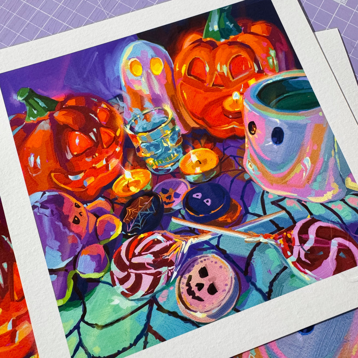 A high-quality physical fine art print on textured white paper showing The Reunion, depicting glowing jack-o'-lantern pumpkins, ghost figurines, a ghost mug, candy, and candles painted in vibrant purple, orange, and mint tones.