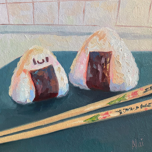 Original oil painting by Alai Ganuza titled "Onigiri/Rice balls". Two triangular rice balls with dark seaweed wraps—one with a cute smiley face—resting on a dark teal surface with decorated wooden chopsticks.