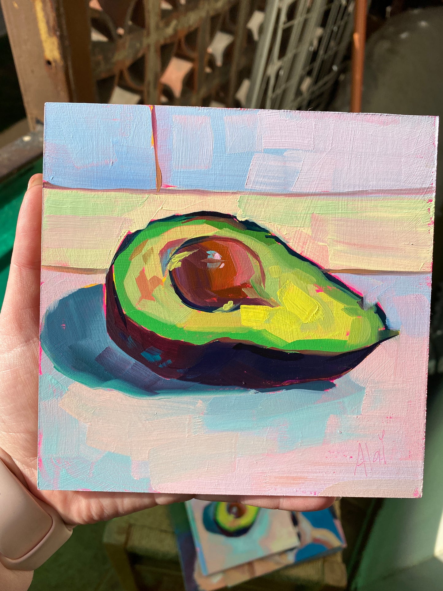 Original oil painting by Alai Ganuza titled "Avocado study II". A ripe avocado half with a large pit, painted with thick impasto in shades of lime green and yellow against a soft, multi-colored pastel background.