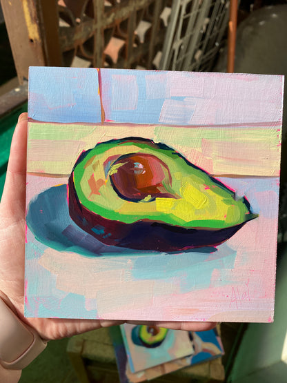 Original oil painting by Alai Ganuza titled "Avocado study II". A ripe avocado half with a large pit, painted with thick impasto in shades of lime green and yellow against a soft, multi-colored pastel background.