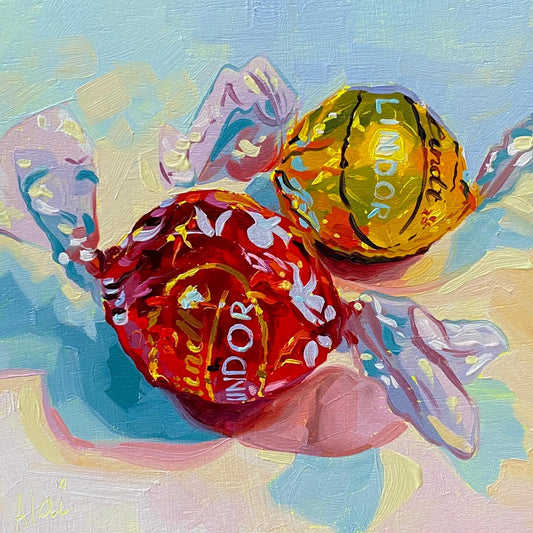 Original oil painting by Alai Ganuza titled "Lindt chocolates III". Two Lindor truffles, one in a red wrapper and one in a yellow wrapper, rendered in thick impasto with cyan and white highlights casting pink and blue shadows.