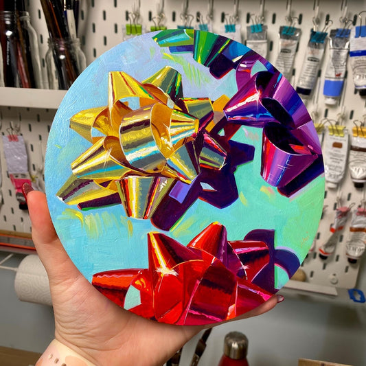Original oil painting by Alai Ganuza titled "Round Bows". Three metallic gift bows—gold, purple, and red—painted with realistic reflections on a round light blue birch wood panel.
