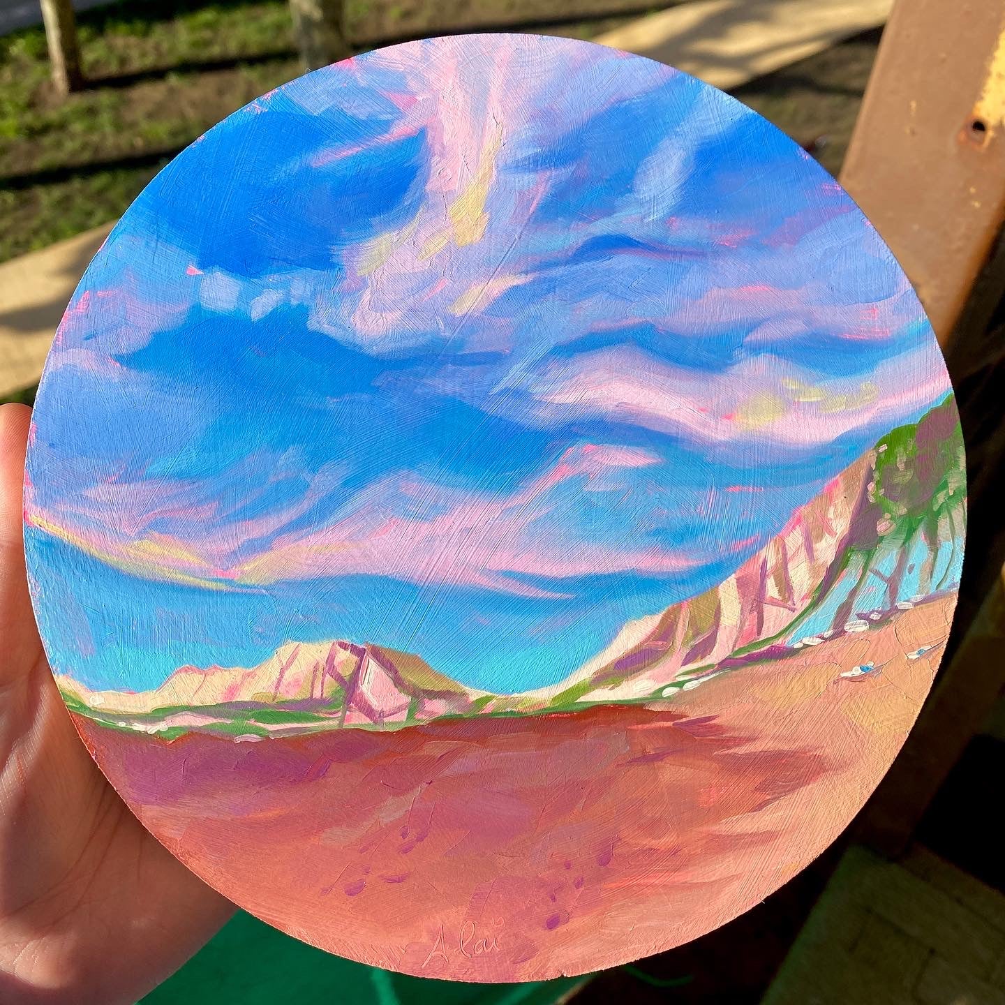 Original circular oil painting by Alai Ganuza titled "Beach Sky". A coastal landscape with a vibrant blue and pink sunset sky, distant mountains, and warm sand, rendered in thick impasto brushwork.